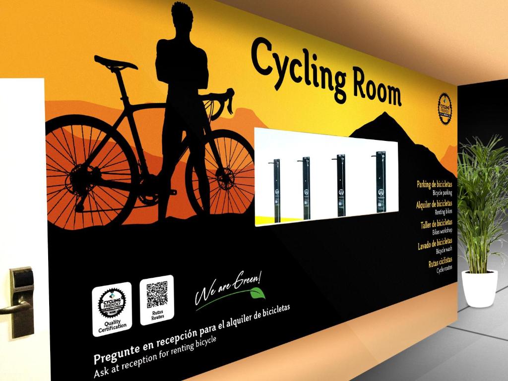 Velosipēdu istaba ar stilizētu sienu dizainu, kurā attēlots velosipēdists un informācija par pakalpojumiem, piemēram, velosipēdu nomu un apkopes darbnīcu. Sienā ir QR kods un uzraksts "We are Green!".