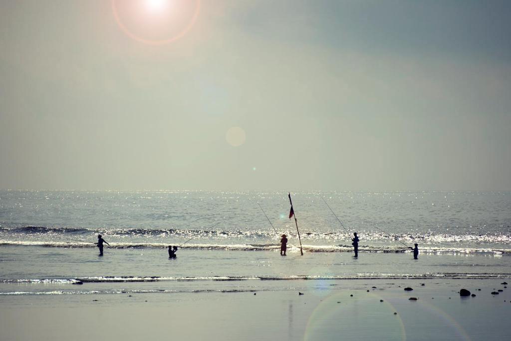 Pludmalē cilvēki zvejo, saulē mirdzošā jūras ūdenī. Sēdēšana krastā un zveja rada mierīgu un relaksējošu atmosfēru.