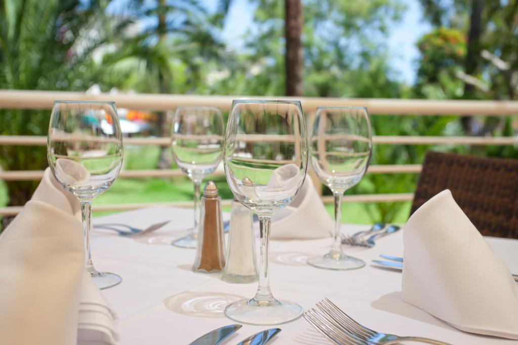 Galda uzstādījums ar glāzēm, galda piederumiem un salvešu locījumiem, kas atrodas ārā, apkārt zaļām ainavām.