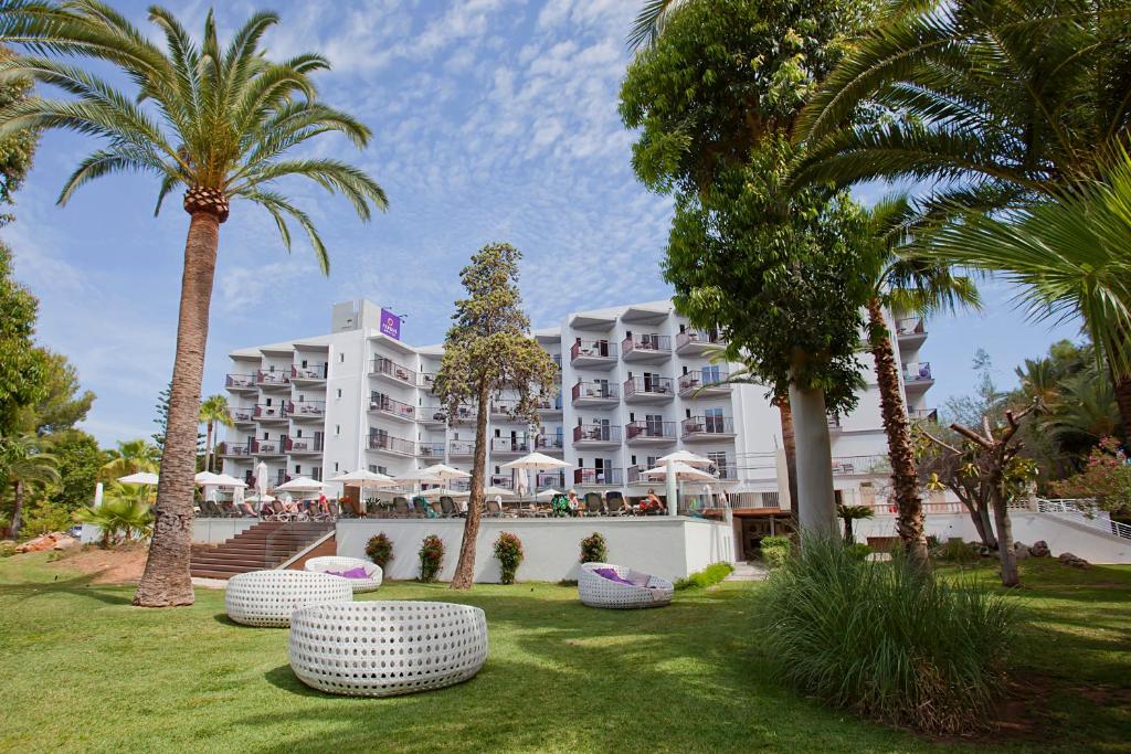 Viesnīcas ēka ar terasēm un palmām, ieskauta zaļā zālē, radot relaksējošu atmosfēru. Ideāla vieta atpūtai un brīvdienām.