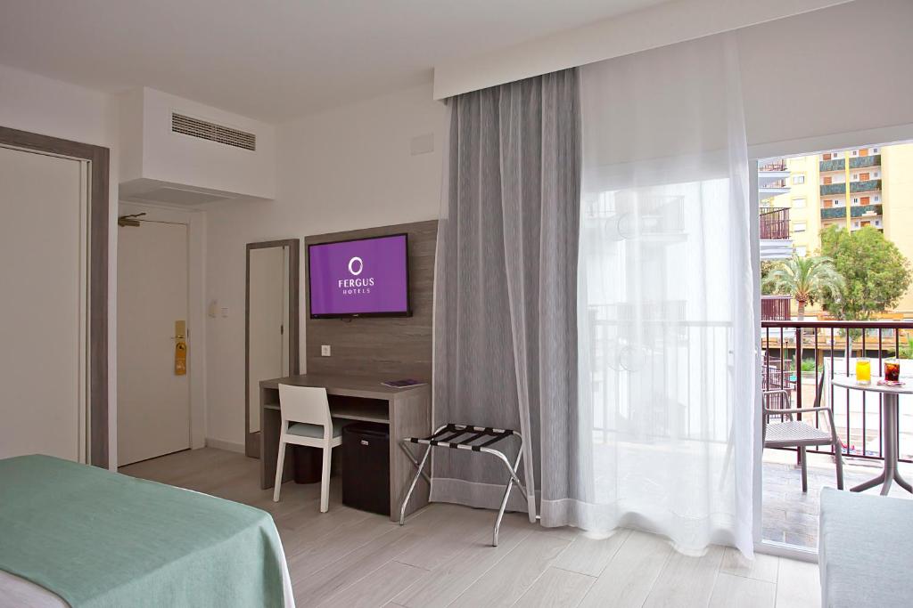 Mūsdienīga viesnīcas istaba ar televizoru un balkonu, kurā ir skatā uz dārzu. Gaismas krāsās veidota interjera dizains rada mājīgu atmosfēru.