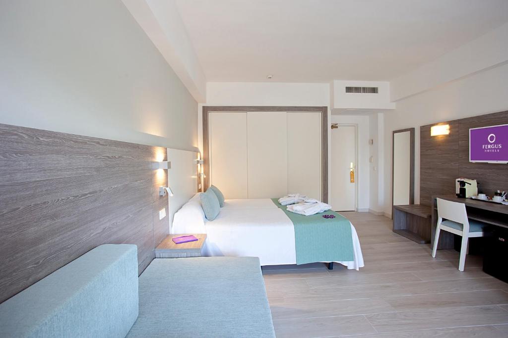 Mūsdienīga viesnīcas numura iekārtojums ar baltām un pelēkām krāsām, kas ietver gultu ar spilveniem, dīvānu un rakstāmgaldu. Numurā ir arī TV un kafijas automāts.