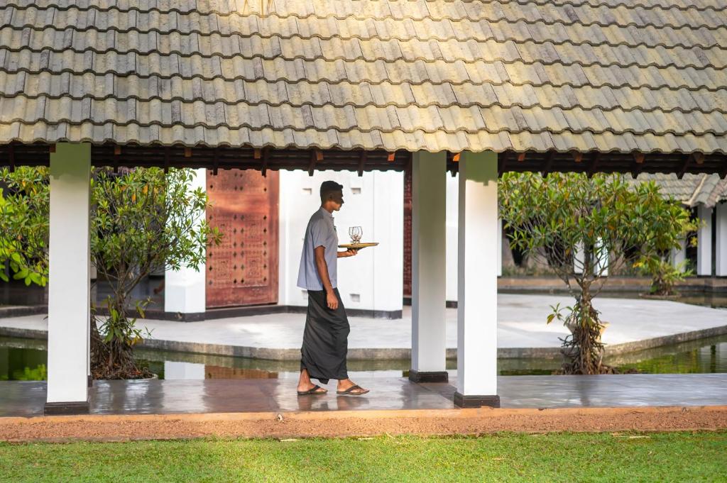 Viesmīlis nēsā pasniegšanas trauku, staigājot pa elegantā kūrorta pagalmu ar zaļu zāli un estētisku arhitektūru.