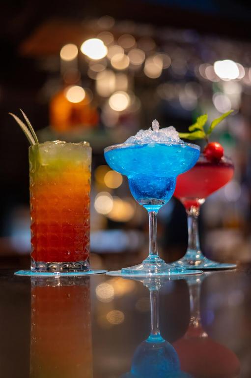 Krāsaini kokteiļi uz bāra letes, ietverot dzērienus ar ledus un augļu rotājumiem. Dzērieni ir dažādu krāsu, radot svinīgu atmosfēru.