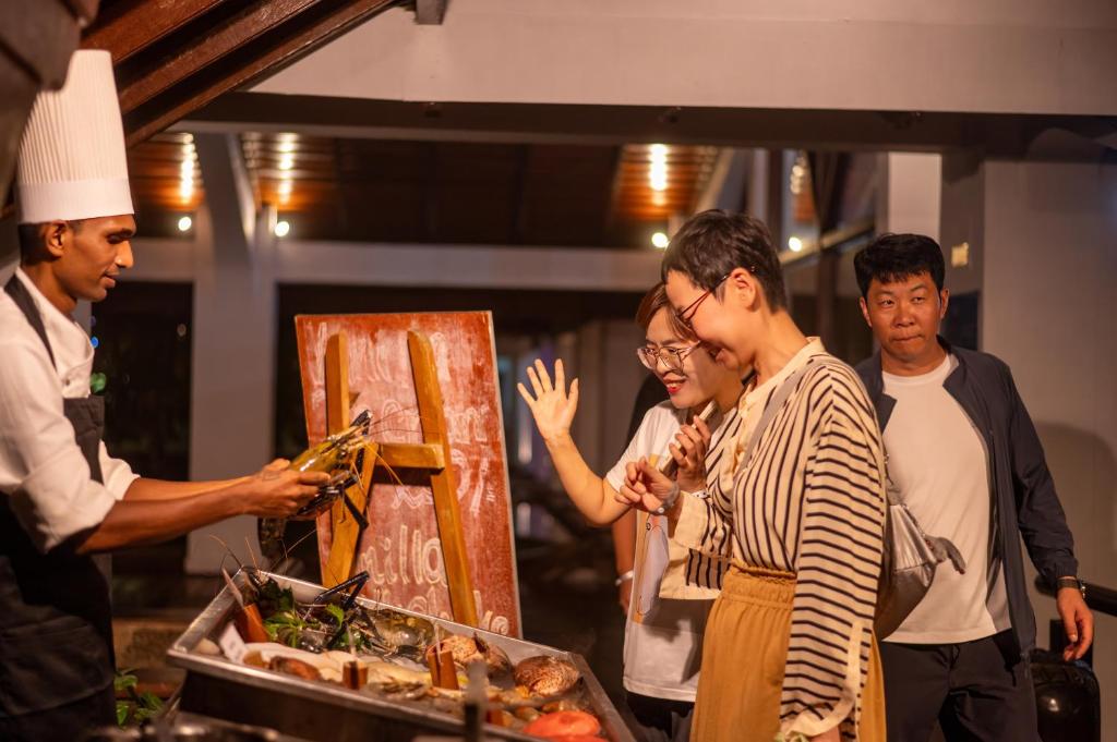 Restorāna šefpavārs piedāvā jūras veltes apmeklētājiem, kuri priecīgi izskata izvēli un sarunājas.