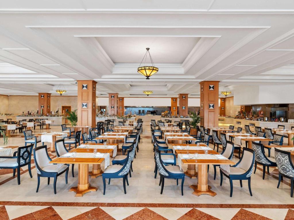 Plaša, moderna restorāna iekšpuse ar elegantiem galdiem un krēsliem, kas izveidoti komfortablai ēšanai. Interjers ietver gaišus toņus un dekoratīvus elementus, radot viesmīlīgu atmosfēru.