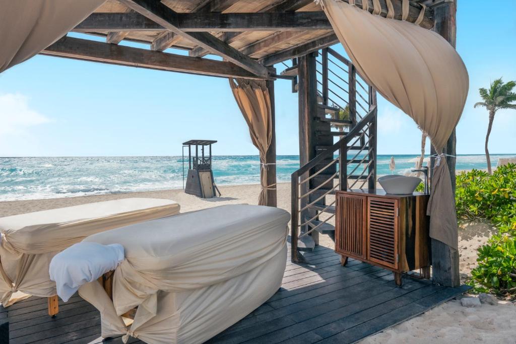 Pludmales spa zona ar masāžas galdiem un skatu uz jūru, kas rada relaksējošu atmosfēru. Koka konstrukcija un dabīgās krāsas papildina mierīgumu.