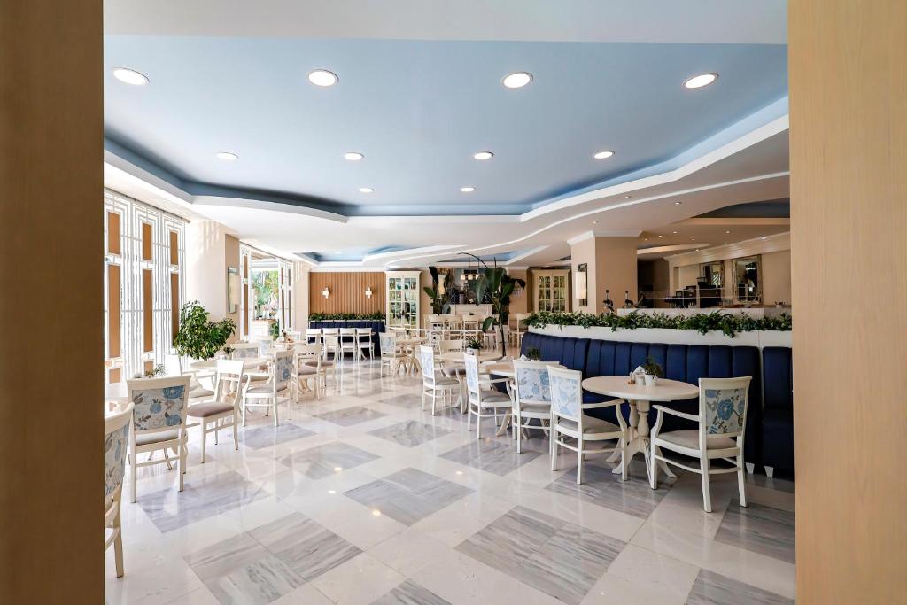 Gaiša un mūsdienīga restorāna interjers ar elegantiem galdiem un krēsliem, apvienojot zilu un baltu krāsu paleti. Labi apgaismota telpa ar augu elementiem un plašām logu rindām, kas nodrošina dabisko gaismu.