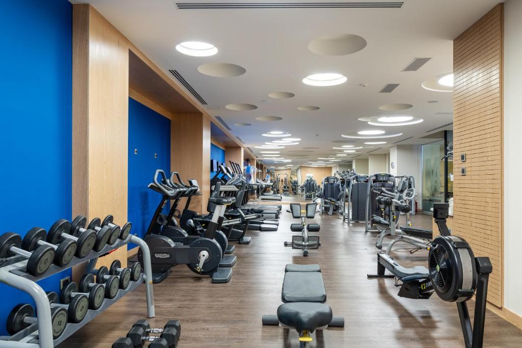Mūsdienīgs sporta zāles iekārtojums ar dažādām trenažieriem un svaru komplektiem, kas veidots ar gaišām krāsām un funkcionālu dizainu.