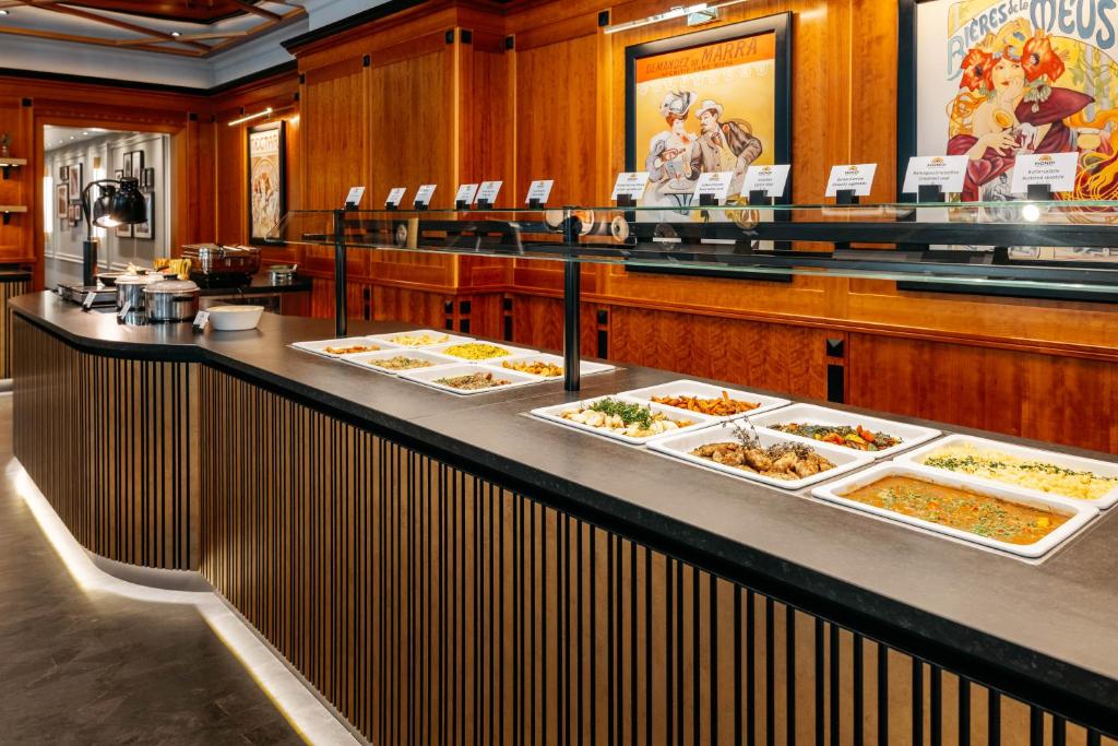 Mūsdienīgs bufetes stends ar dažādiem ēdieniem, kas izkārtoti uz melna galda. Fons rotā klasiskas mākslas gleznas, radot siltu un viesmīlīgu atmosfēru.