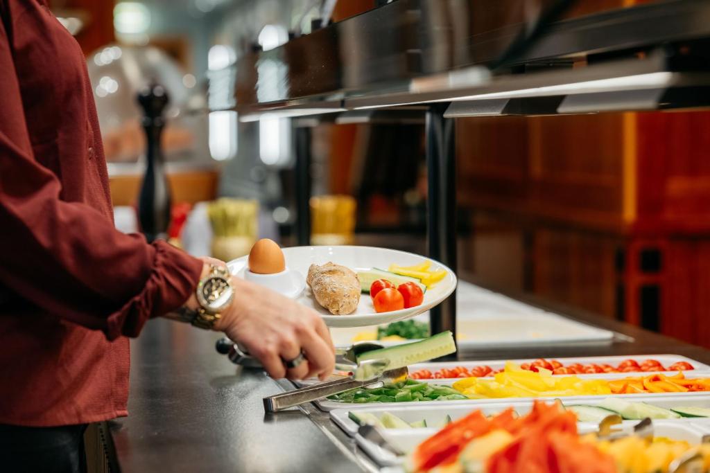 Pusdienu bufete ar dažādiem dārzeņiem un augļiem, kurā cilvēks izvēlas ēdienu no plāksnes.