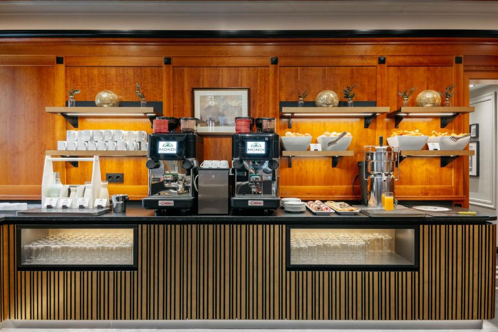 Kafijas stends ar modernām iekārtām, ko ieskauj eleganta koka apdare un dekoratīvi elementi, piedāvā dažādus dzērienus un uzkodas.