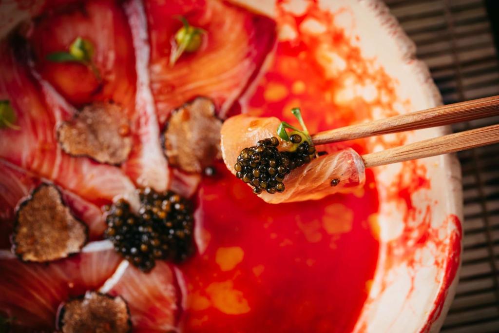 Svaiga sushi šķēle ar kaviāru, pasniegta uz krāsainas šķīvja ar garšaugiem.