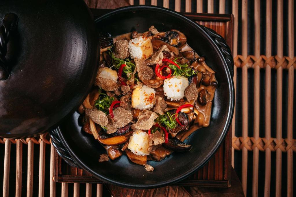 Gourmet ēdiens ar sēnēm, rīsiem, trifelēm un zaļajiem sīpoliem, pasniegts melnā traukā. Ideāla izvēle gardēžiem, kas novērtē izsmalcinātu garšu.