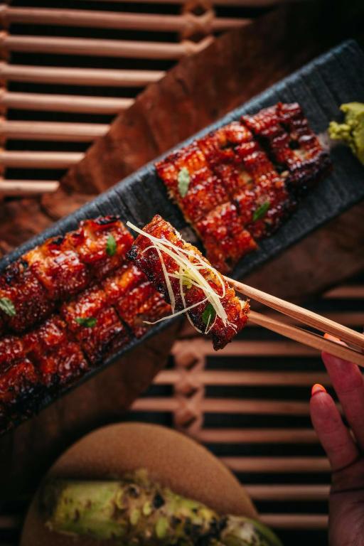 Grilēts zivs filejas gabals ar glazūru, pasniegts uz melnas akmens plāksnes, kopā ar wasabi un zaļumiem.