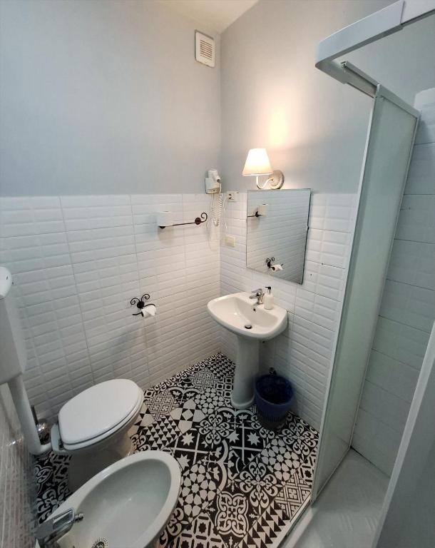 Mūsdienīga vannas istaba ar melnbaltu flīžu grīdu, izlietni, tualeti un dušu. Sienas ir gaiši pelēkas, un telpā ir iekļauta gaisma.