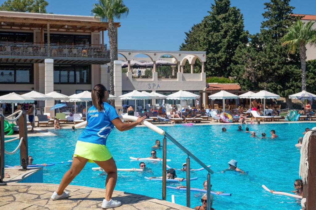 Baseina zona ar animācijas komandas dalībnieku, kas piedalās aktivitātēs, fonā redzama viesnīca un atpūtas zonas ar sauļošanās krēsliem.