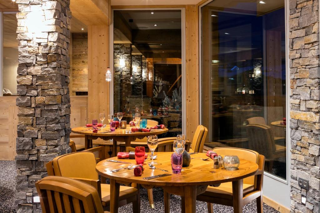 Elegants restorāna interjers ar koka un akmens elementiem, kur ap galdiem ir krāsaini stikla trauki un sveces. Labi apgaismots un aicinošs noskaņojums.