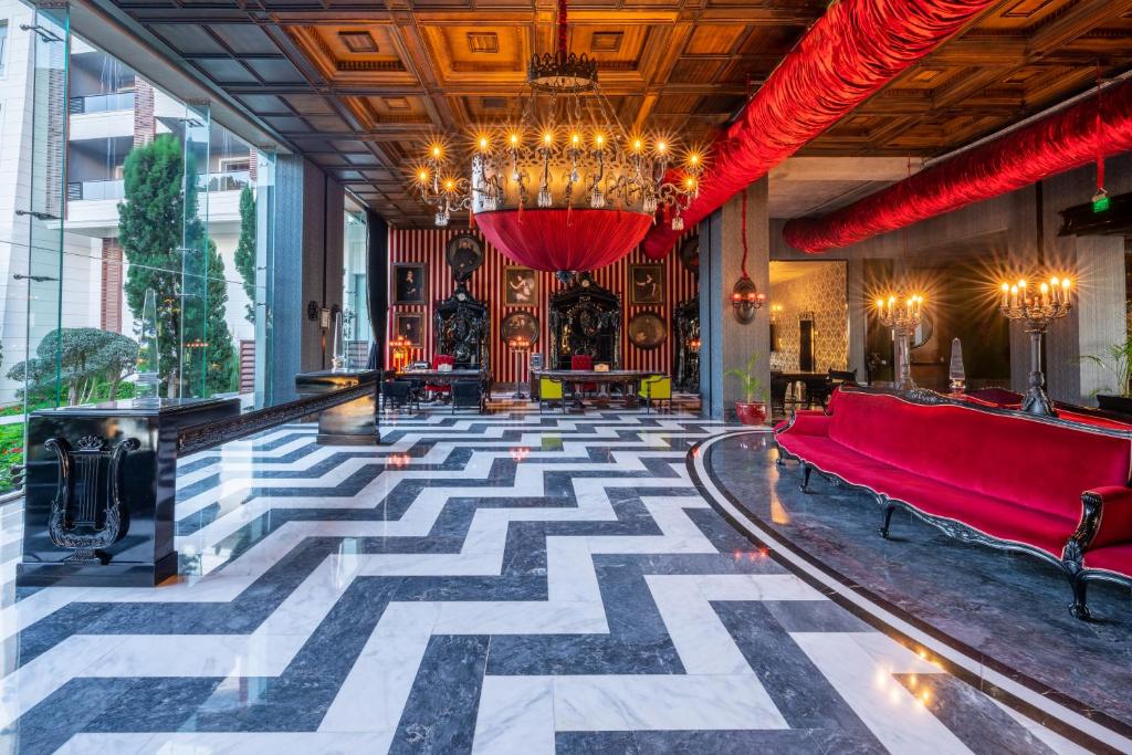 Elegants viesnīcas interjers ar melnbaltu grīdu, greznām sarkanām dīvāniem un izsmalcinātu lustru. Moderns dizains apvieno klasiskos elementus un mūsdienīgus akcentus.