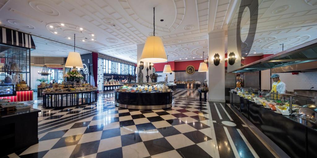 Mūsdienīgs bufete ar elegantu interjeru, kurā ir dažādi ēdieni un dzērieni, izgaismoti ar lielām lampām. Grīdas dizains ir melnbalts, radot stilīgu atmosfēru.