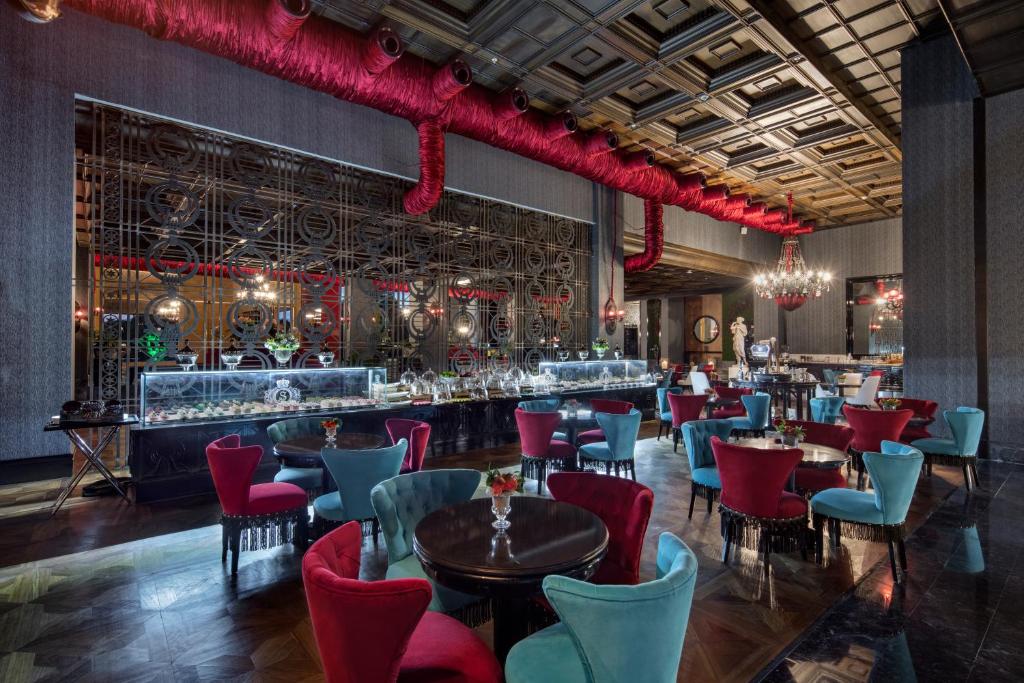 Elegants restorāns ar moderna dizaina interjeru, kurā redzami krāsaini krēsli un grezna gaismekļu apgaismojums. Uz galds ir izkārtota bufete ar dažādiem ēdieniem.