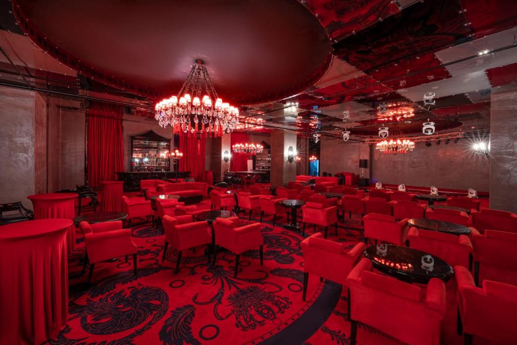 Elegants sarkans interjers ar greznu lustru un komfortablām sēdvietām. Telpa ir apgaismota ar sarkaniem gaismas avotiem, radot intīmu atmosfēru.