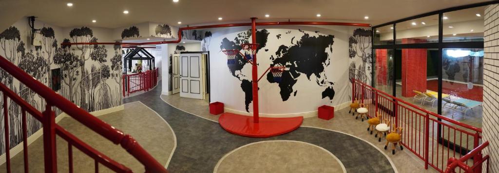 Mūsdienīgs interjers ar melnu pasaules karti uz sienas un sarkaniem akcentiem, veidojot dinamisku un radošu telpu. Redzami arī dažādi sēdvietu risinājumi un dekoratīvi elementi.