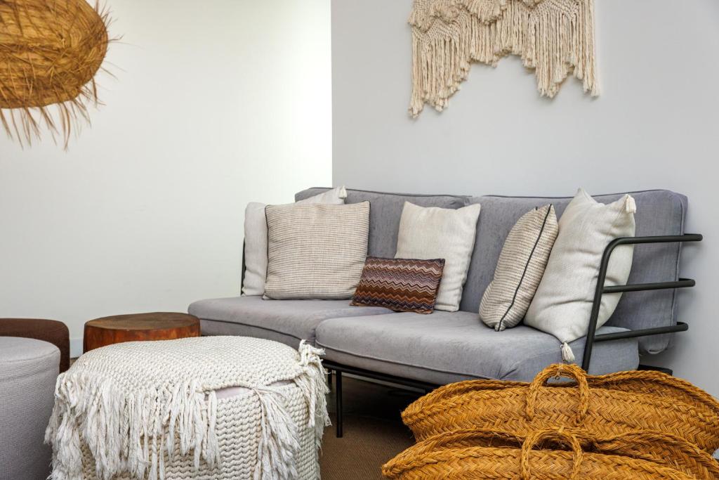 Mūsdienīgs dzīvojamās istabas stūris ar pelēku dīvānu, dekoratīviem spilveniem un dabīgām rotājumu detaļām. Siltas krāsas un tekstūras rada mājīgu atmosfēru.