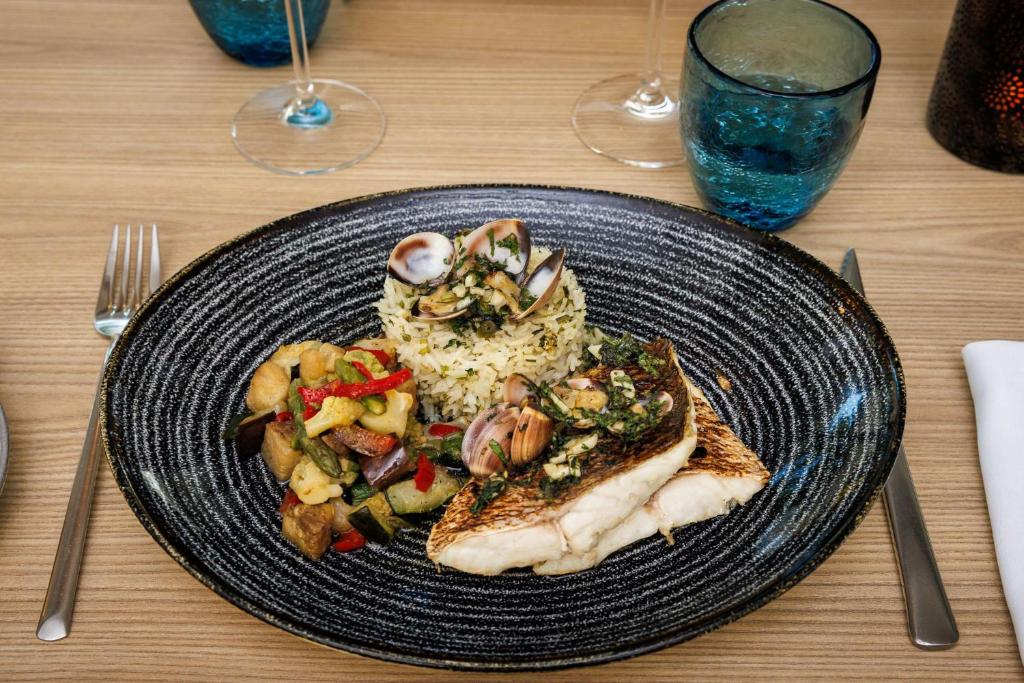 Garšīgi pasniegts cepts zivs filejas gabals ar garšaugiem, rīsiem un dažādām dārzeņu garnējumu. Ideāls ēdiens, kas apvieno jūras veltes un dārzeņu svaigumu.