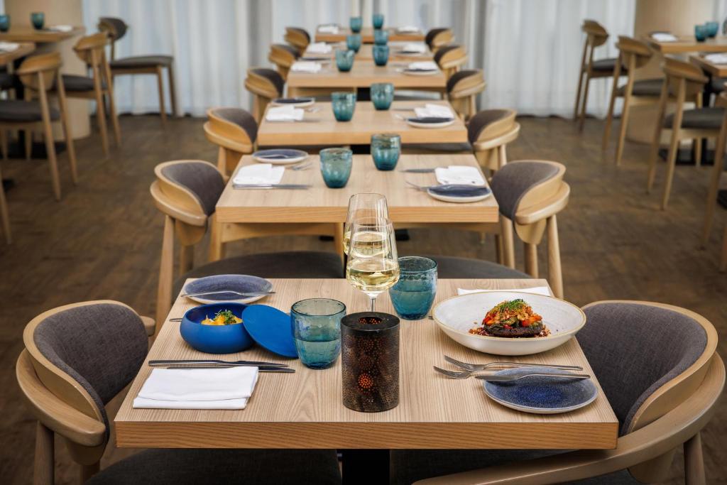 Elegants restorāna interjers ar koka galdiem un krēsliem, kurā ir pasniegti dažādi ēdieni un dzērieni. Gaisma un elegantas detaļas rada patīkamu atmosfēru.