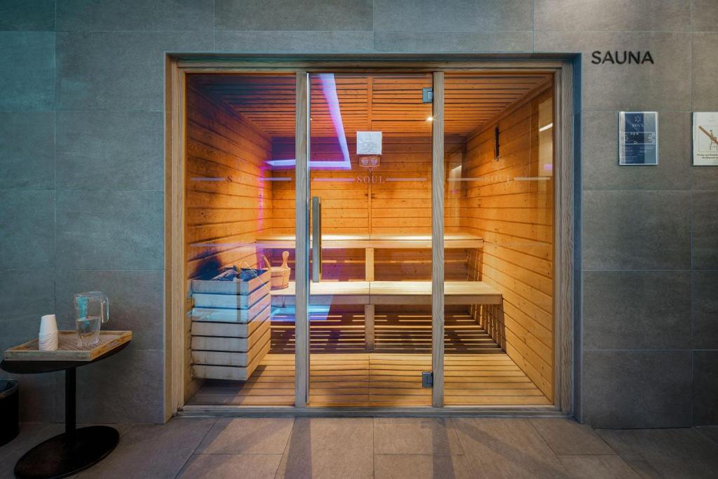 Mūsdienīga sauna ar koka interjeru un krāsainu apgaismojumu, kas aicina uz relaksāciju. Blakus ir galds ar ūdens krūzi un vienreizējām glāzēm.