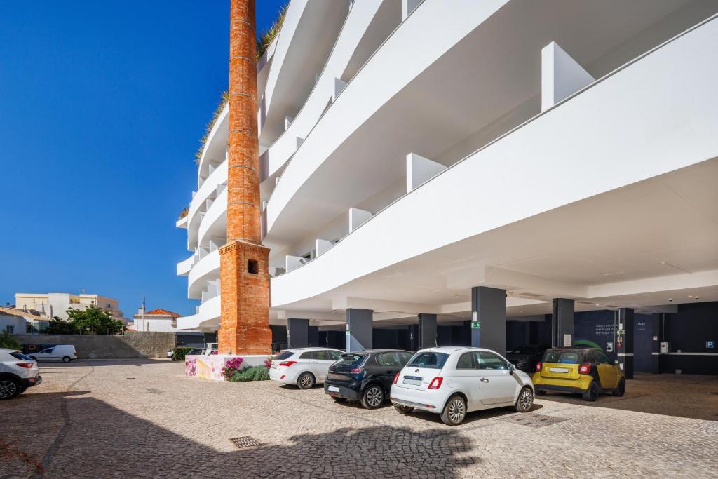 Mūsdienīga ēka ar plašu autostāvvietu, kurā redzami dažādi automobiļi un izteikta ķieģeļu skursteņa konstrukcija. Skats uz skaidru zilu debesu fonu.