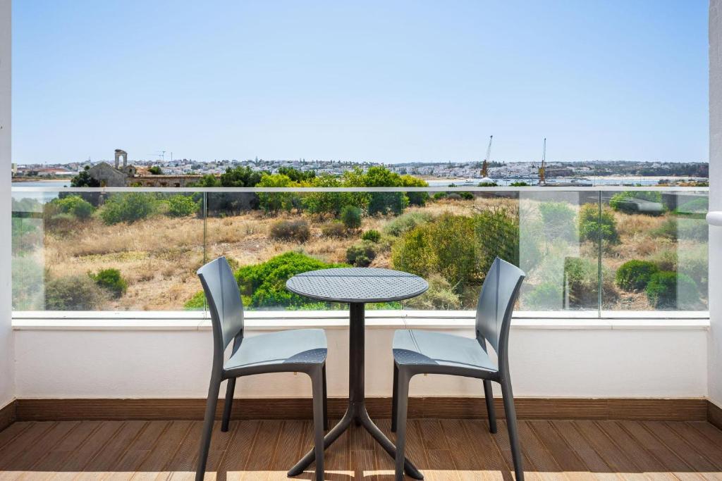 Terase ar skatu uz ainavu, kurā redzama zaļa veģetācija un tālāk esoši būvniecības elementi. Uz terases atrodas divi pelēki krēsli un apaļa galda.