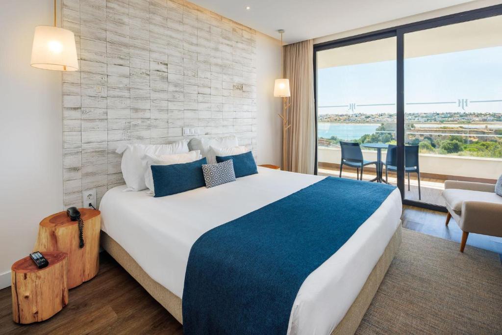 Mūsdienīgs viesnīcas numurs ar plašu gultu un skatu uz ainavu. Interjerā ir koka elementi un gaiši toņi, radot relaksējošu atmosfēru.