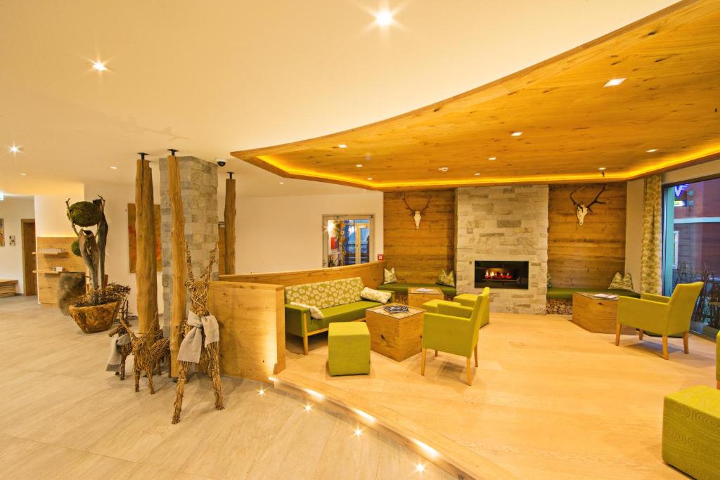 Mūsdienīgs viesnīcas uzgaidāmās telpas interjers ar koka un akmens elementiem, zaļām mēbelēm un kamīnu, radot siltu un viesmīlīgu atmosfēru.