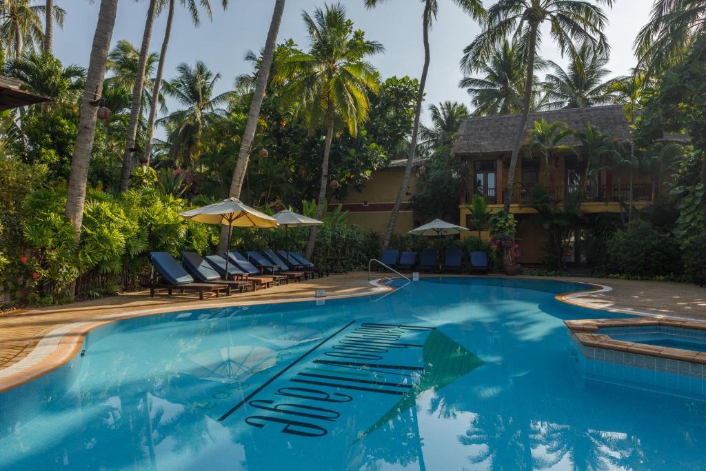 Peldbaseins ar saulessargiem un sauļošanās krēsliem, ieskauts tropiskajā ainavā ar palmām un zaļumiem. Ideāla vieta relaksācijai un atpūtai.