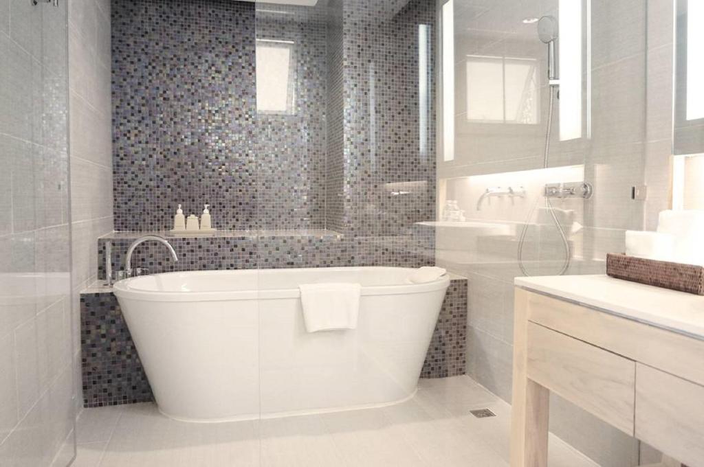 Mūsdienīga vannas istaba ar elegantu brīvo stūra vannu, flīzēm ar mozaīkas rakstu un modernu apgaismojumu. Interjers ir gaišs un elegants, radot relaksējošu atmosfēru.