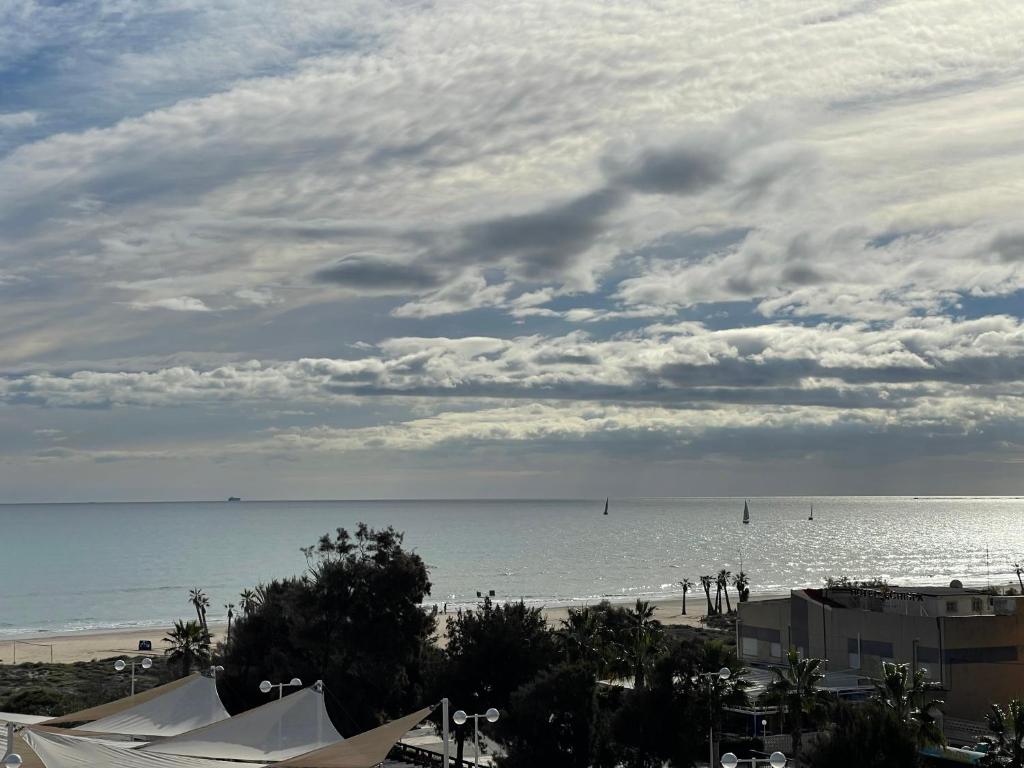 Jūras ainava ar burājošiem kuģiem, saulainu debesi un mīkstiem mākoņiem. Pludmale un palmas pie horizonta rada mierīgu atmosfēru.