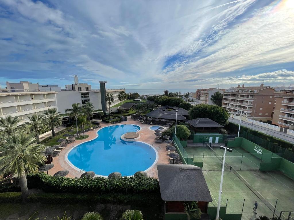 Lieliska ainava ar peldbaseinu, tropiskām palmām un tenisa laukumiem, kas atrodas viesnīcas teritorijā. Fons papildināts ar skaidru debesu un jūras skatu.