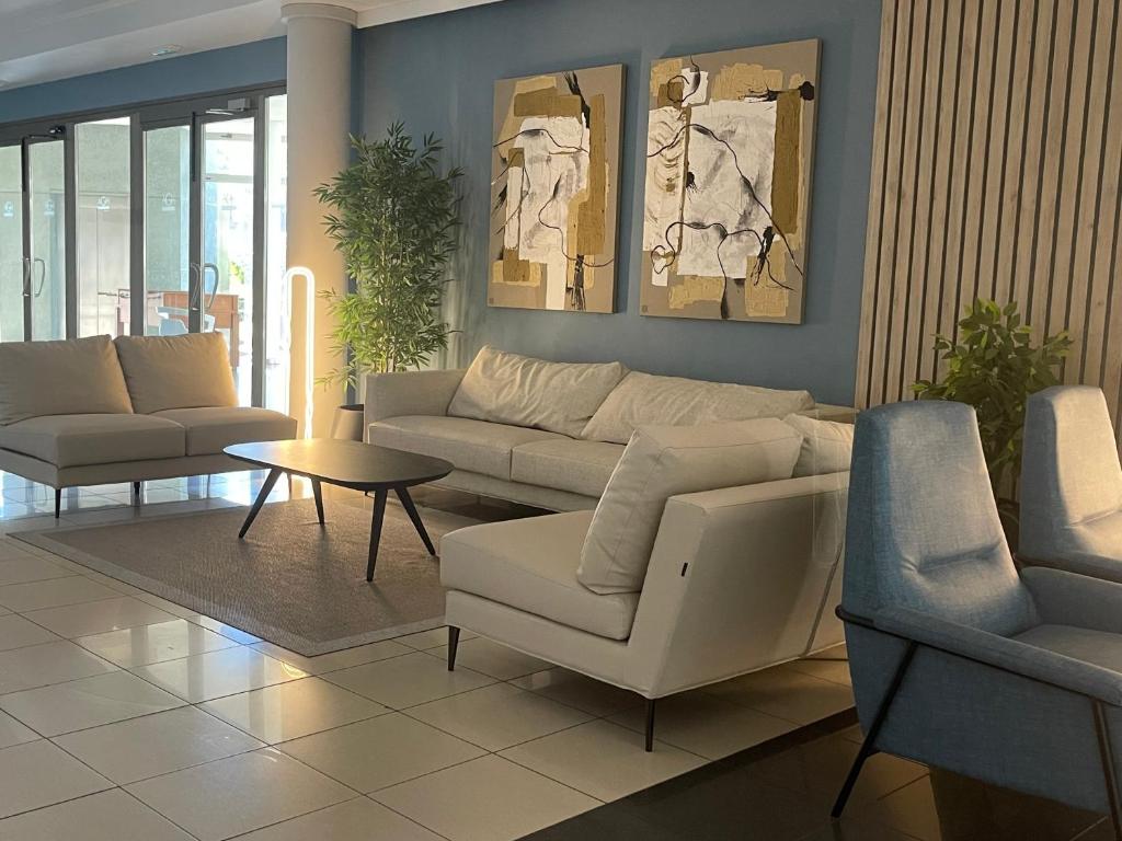 Mūsdienīgs viesnīcas interjers ar gaišiem dīvāniem, melnu kafijas galdiņu un mākslas darbiem uz sienas. Apkārt ir augi un liels logs, kas nodrošina dabisko apgaismojumu.