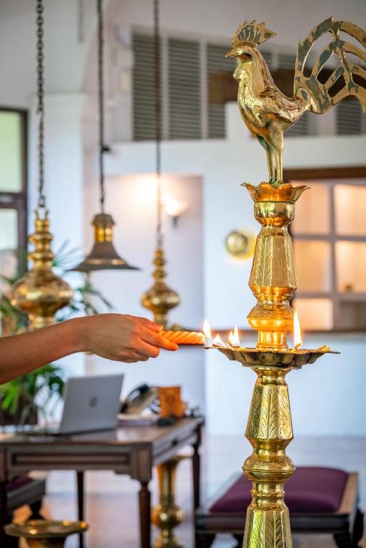 Zelta svečturis ar gaišām svecēm un roosters kā dekorāciju, kas atrodas viesnīcas vestibila apgaismojumā.