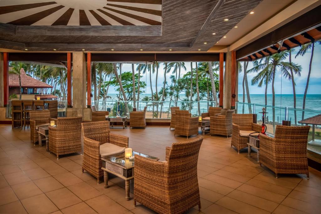 Moderns atpūtas telpa ar skatu uz pludmali, kur ir izkārtoti vītņu krēsli un galdi, radot relaksējošu atmosfēru. Iespaidīgais interjers un dabas elementi rada ideālu vidi atpūtai.