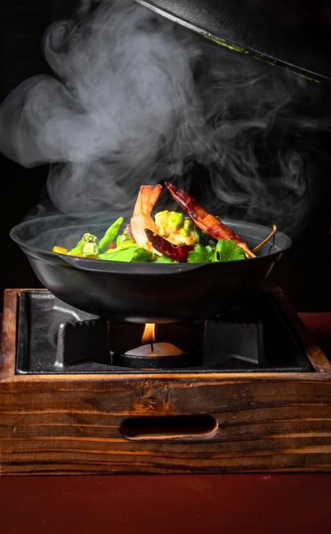 Dūmu mākonis paceļas no melnas pannu ar garnelēm un dārzeņiem, kas pasniegti uz koka statīva. Dish izskatās garšīgi un pievilcīgi.