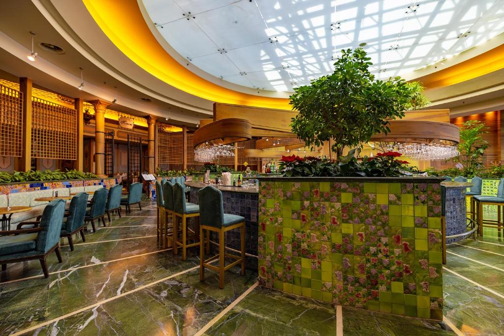 Moderns restorāns ar zaļiem akcentiem un elegantiem interjera elementiem, kurā ir bārs un plašas sēdvietas. Gaismas un augu kompozīcija rada patīkamu atmosfēru.