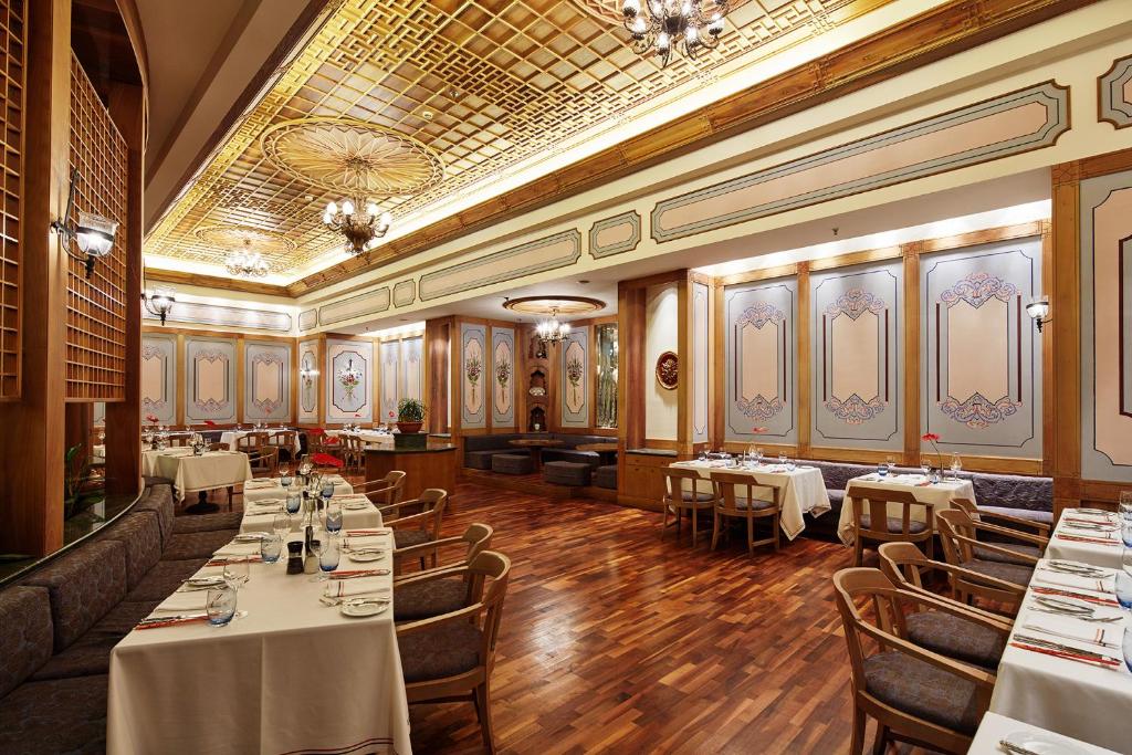 Elegantā restorāna iekārtojums ar izsmalcinātu apgaismojumu un rotājumus uz sienām. Galds klāts ar baltām galdautām un zilo trauku komplektiem.