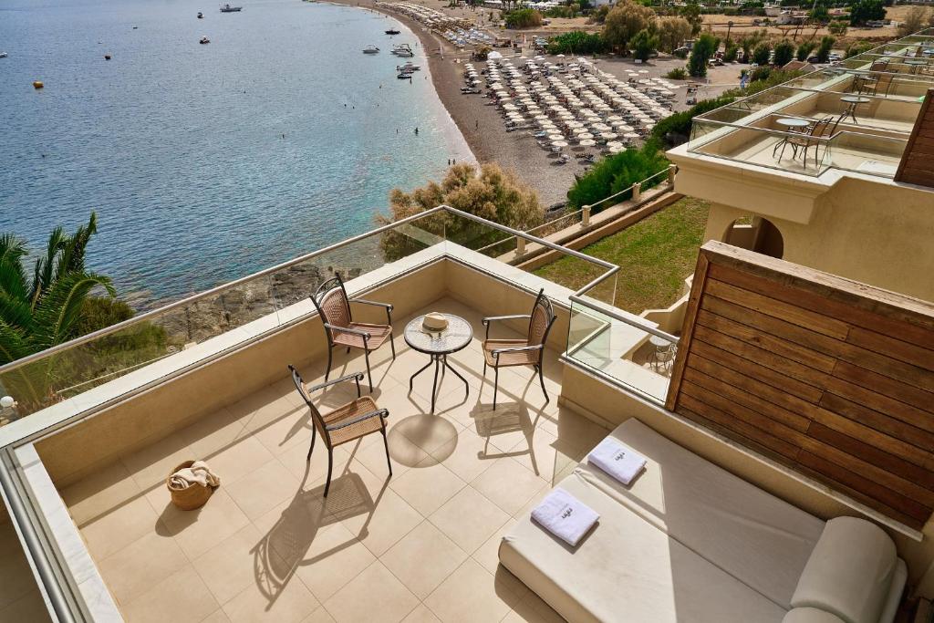 Terase ar skatu uz pludmali un jūru, kurā ir divi krēsli un galds, radot mierīgu atpūtas vietu. Apkārt redzami sauļošanās krēsli un laivas ūdenī.