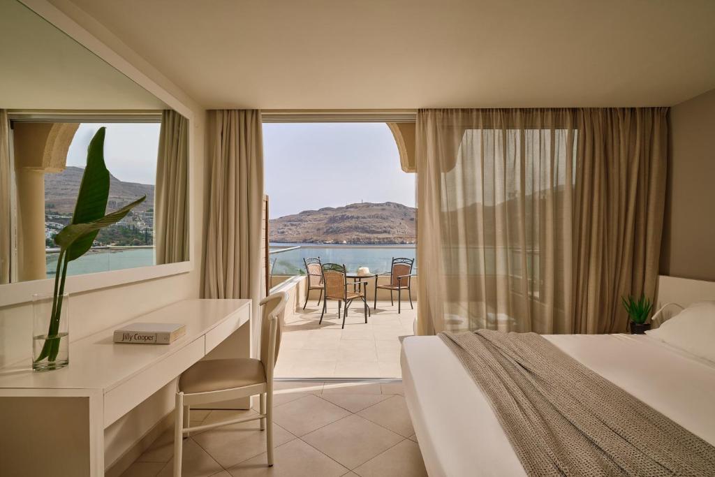 Mūsdienīgs viesnīcas numurs ar skatu uz jūru, kurā ir gulta, rakstāmgalds un terase ar sēdvietām. Interjers ir gaišs un elegants, radot relaksējošu atmosfēru.