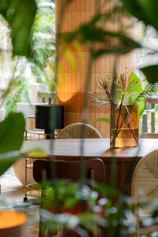 Elegants interjera skats ar koka galdu, ziediem stikla vāzē un zaļām augu lapām, radot relaksējošu atmosfēru. Dabiskais apgaismojums akcentē telpas dizainu.