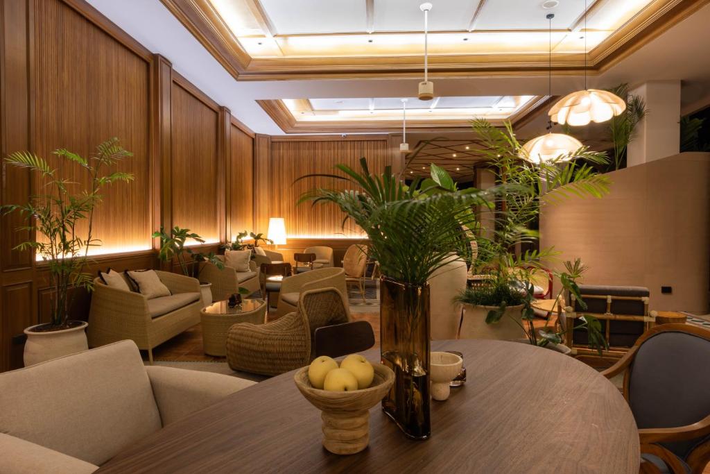 Mūsdienīgs interjers ar koka paneļiem, ērtām mēbelēm un zaļām augu dekorācijām, radot patīkamu un relaksējošu atmosfēru.