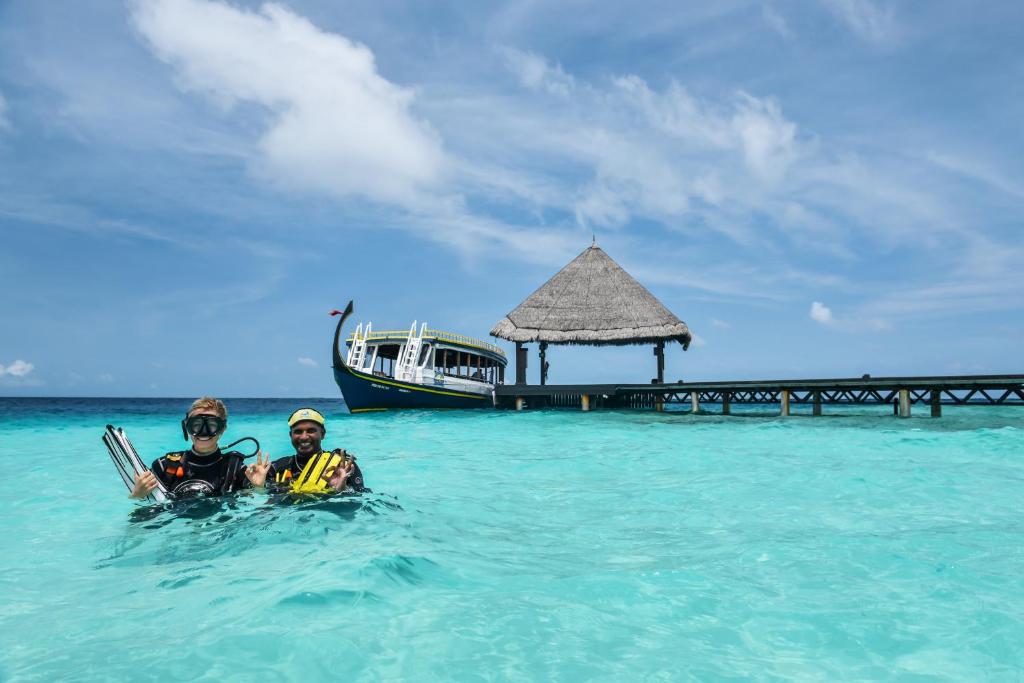 Diving enthusiasts pose in clear turquoise waters, with a boat and a thatched pier in the background. The scene captures the essence of a tropical adventure.
